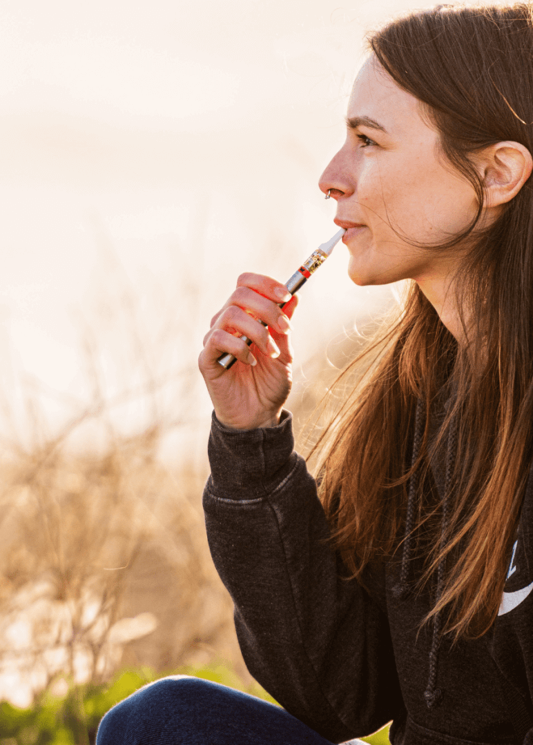 A close up shot of a 510 thread cartridge and a weed pen battery in a woman's mouth while she takes a hit.