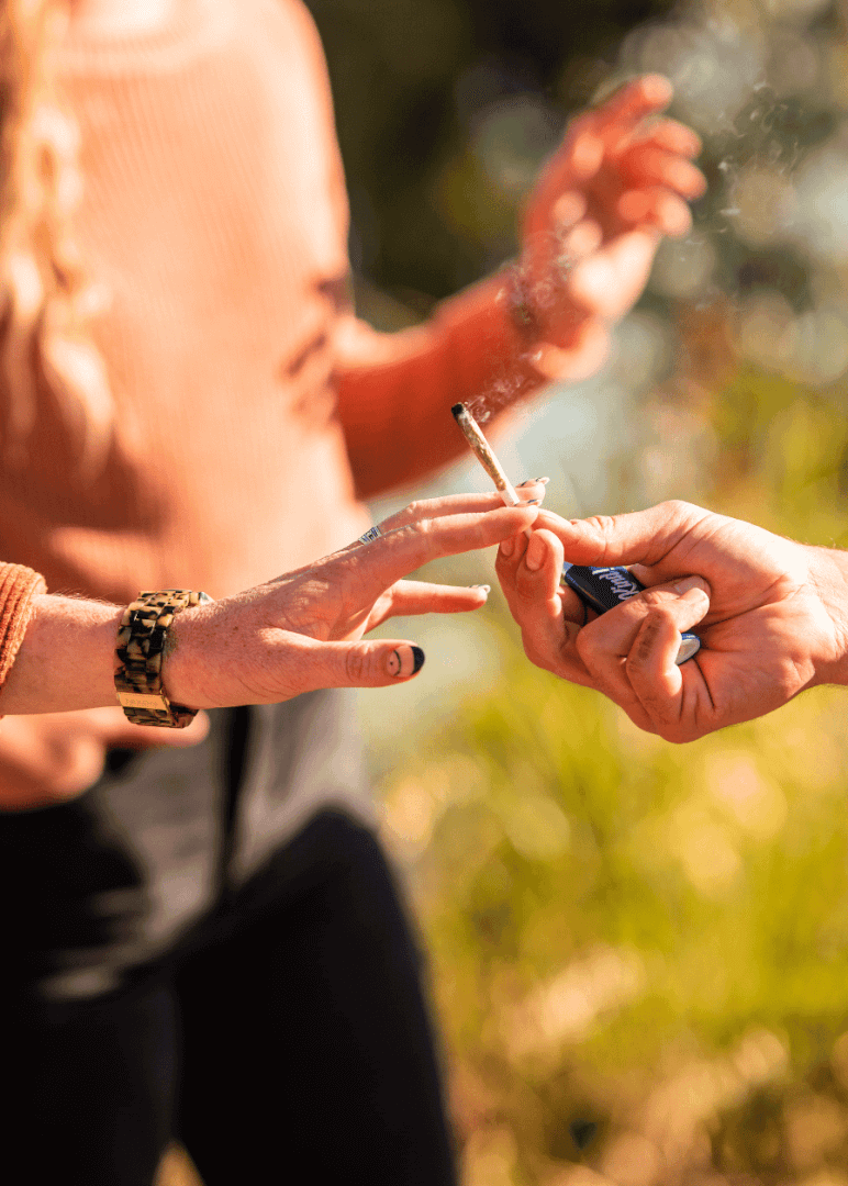 Two people pass a lit infused pre roll from Xzibit's West Coast Cannabis in Marina Del Rey back and forth between each other out in nature.